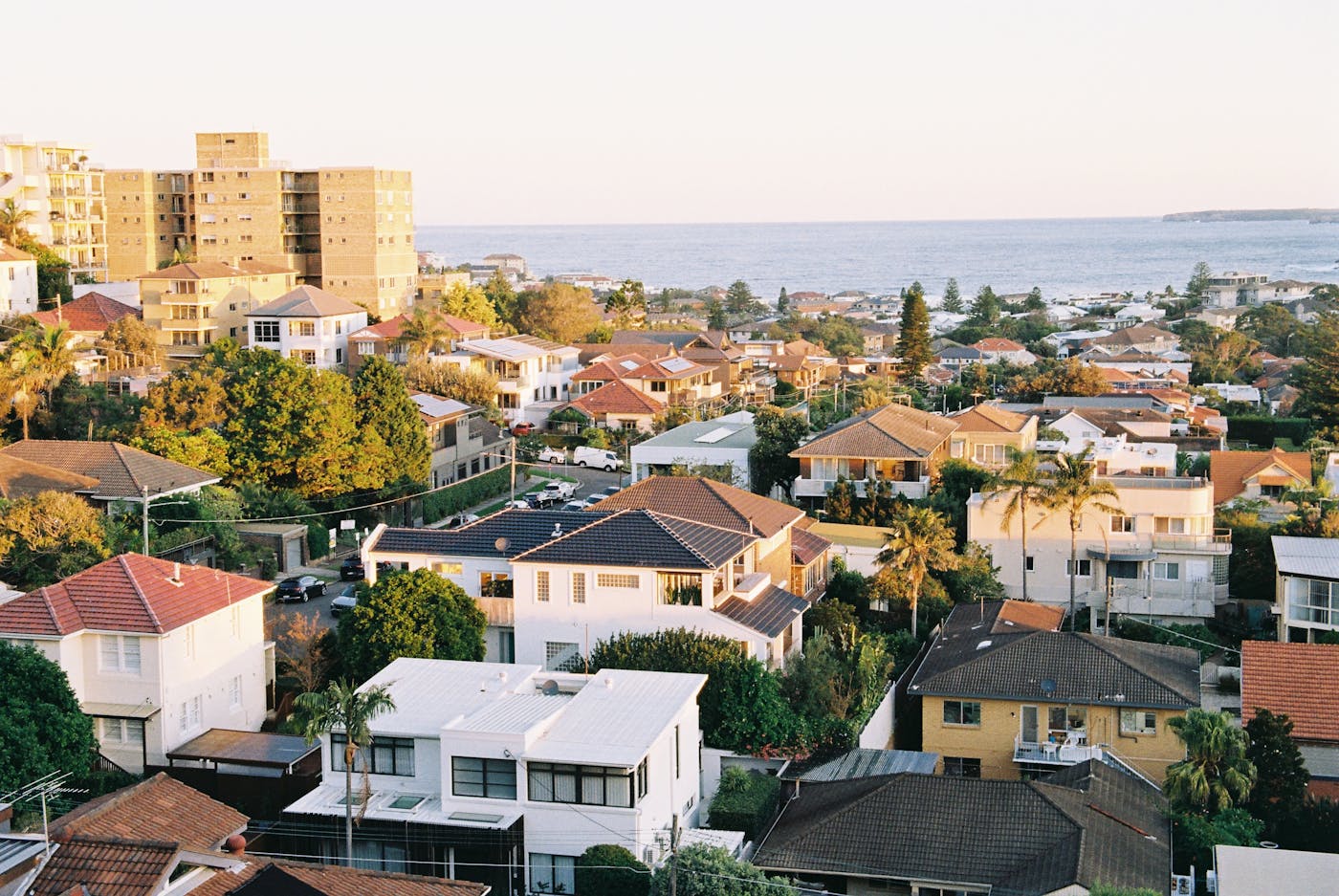 Aerial view of a coastal suburb with colourful houses and ocean horizon at sunset in NSW