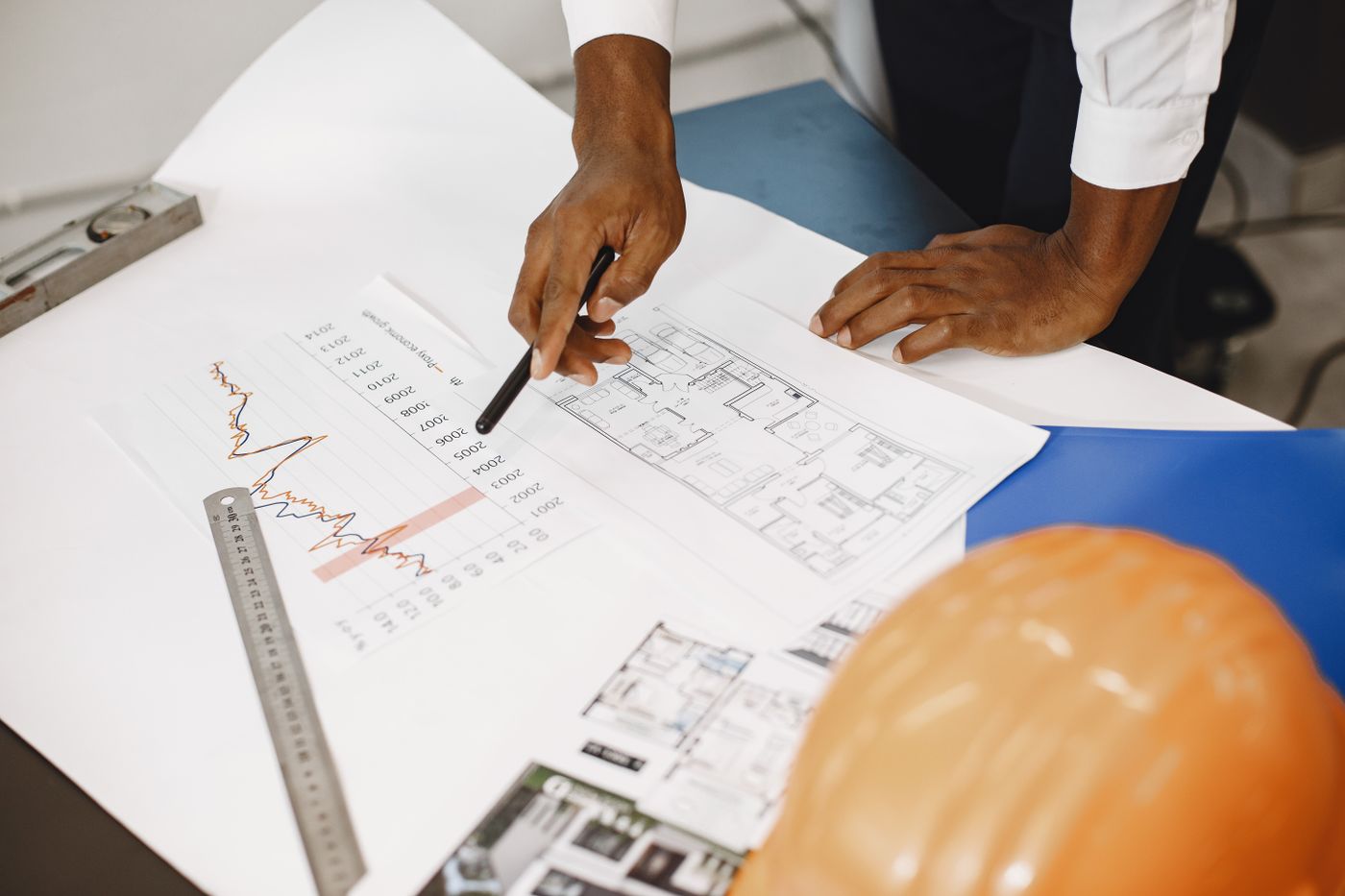 Hands of an architect analyzing blueprints and financial documents at a desk