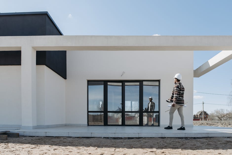 Architect with hard hat reviewing plans at a modern home exterior
