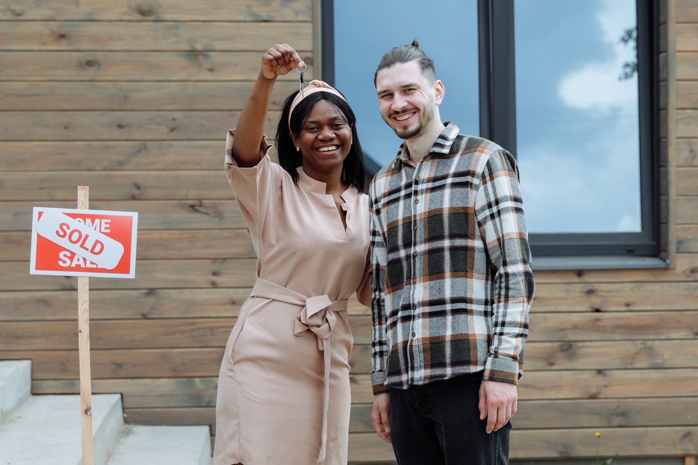 Young couple celebrating their first home purchase with keys and a sold sign